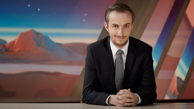 "NEO MAGAZIN ROYALE mit Jan Böhmermann": Jan Böhmermann sitzt mit gefalteten Händen am Schreibtisch und schaut grinsend in die Kamera.