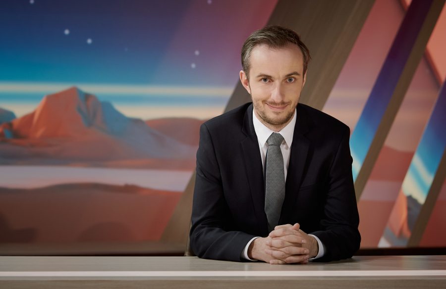 "NEO MAGAZIN ROYALE mit Jan Böhmermann": Jan Böhmermann sitzt mit gefalteten Händen am Schreibtisch und schaut grinsend in die Kamera.